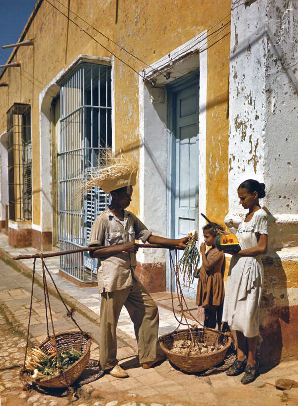 Street vendor holding out onions to a woman holding tropical fruit in Cuba.
