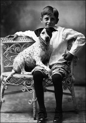 Boy posed with dog on wicker chair (191-)