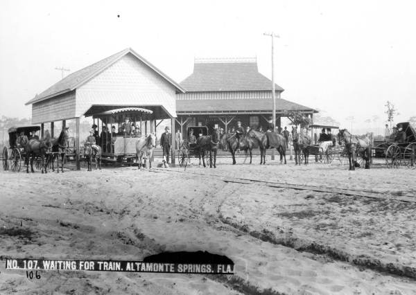 People in horse-drawn omnibuses waiting for a train