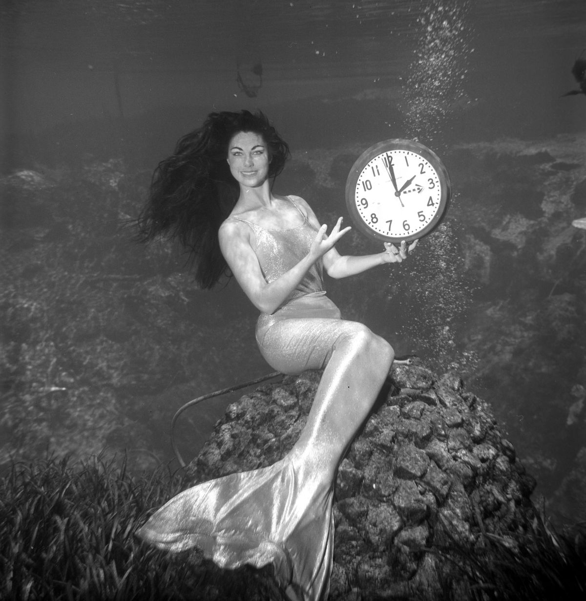 Weeki Wachee mermaid Peggy, underwater in her tail costume, with clock for a "Time change" shoot.