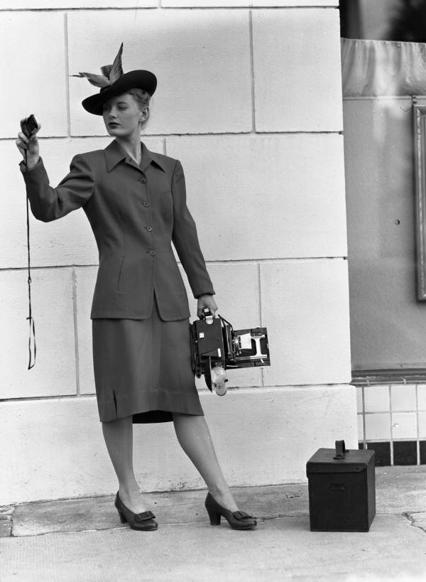 Model holding a Speed Graphic camera while viewing a light meter.