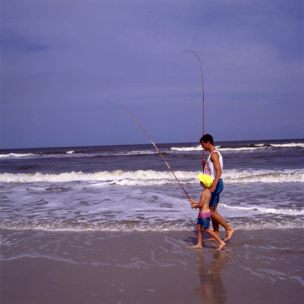 Father and son at the beach with their fishing poles.