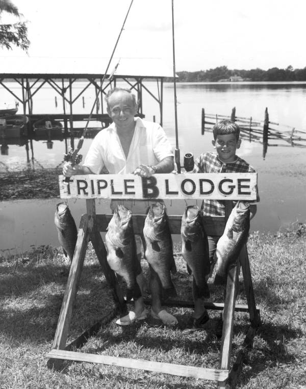T. E. Dodamead and his son Tom pose with their catch of bass hanging from the Triple B Lodge sign - Welaka, Florida.