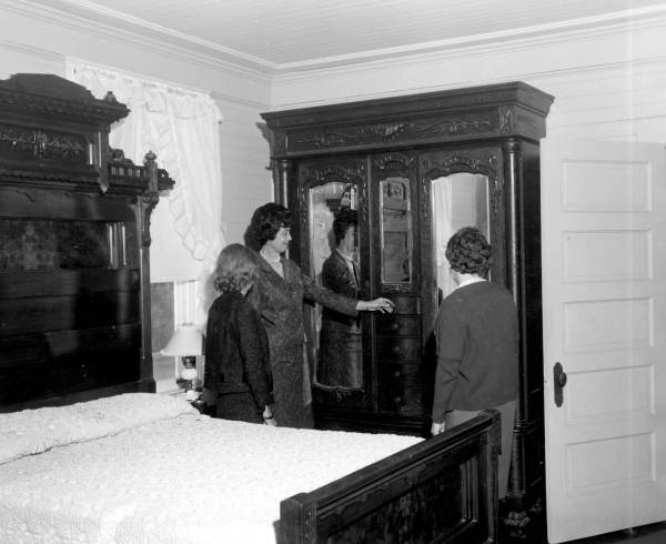 Three women looking at a mirrored armoire in a bedroom - Apalachicola, Florida.