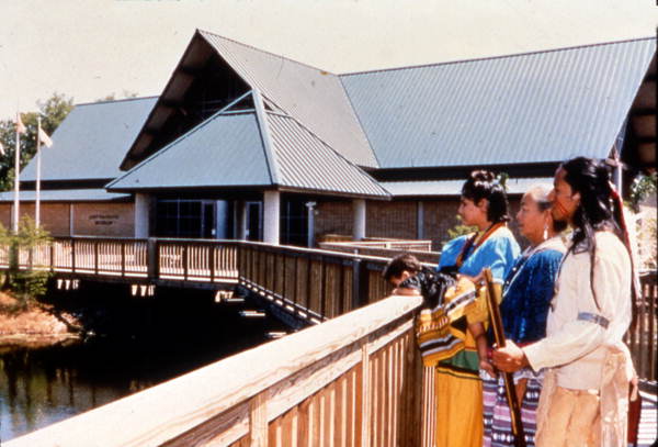 View showing Seminole Indians standing near the Ah-Tah-Thi-Ki Museum of the Seminole Tribe of Florida.