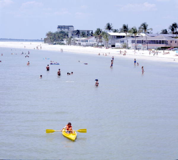 Young man kayaking by people enjoying the beach - Fort Myers, Florida