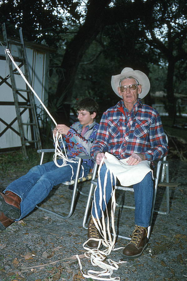 Cow whip maker George "Junior" Mills (r) cuts strips of buckskin while his apprentice J. Taylor Marcus plaits a whip - Okeechobee, Florida.