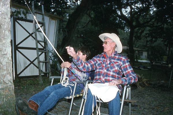 Cow whip maker George "Junior" Mills (r) cuts strips of buckskin while his apprentice J. Taylor Marcus plaits a whip - Okeechobee, Florida.