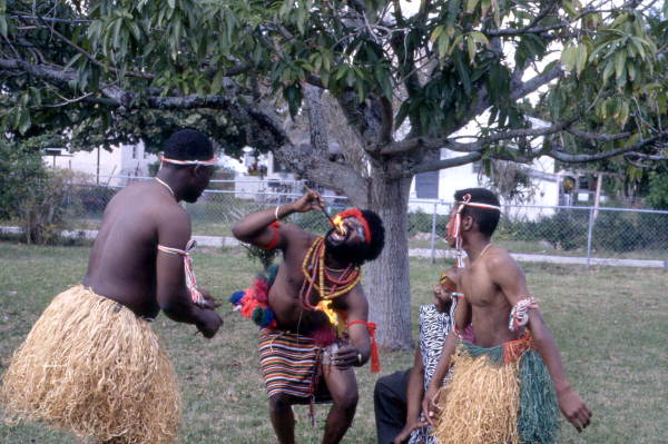 Nigerian acrobatic dancer Augustine Omeben eats fire as Felix Omeben, Akila Baki, and Moses Campbell observe - North Miami, Florida