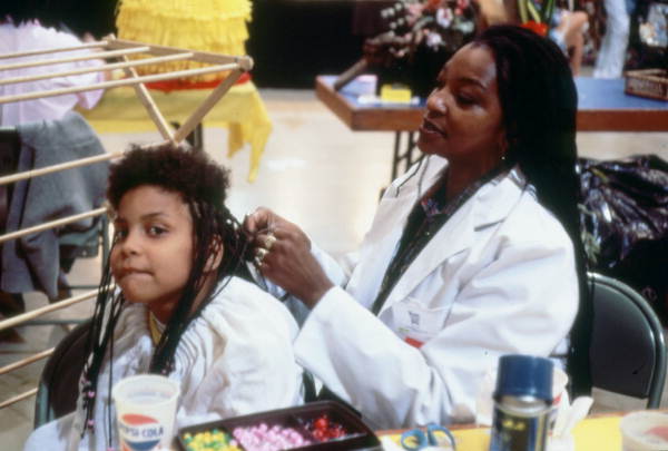 Young girl gets her hair braided .