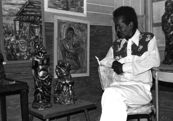 Pharaoh Baker of Lake City posing with sculptures and paintings in the display area of his workshop..