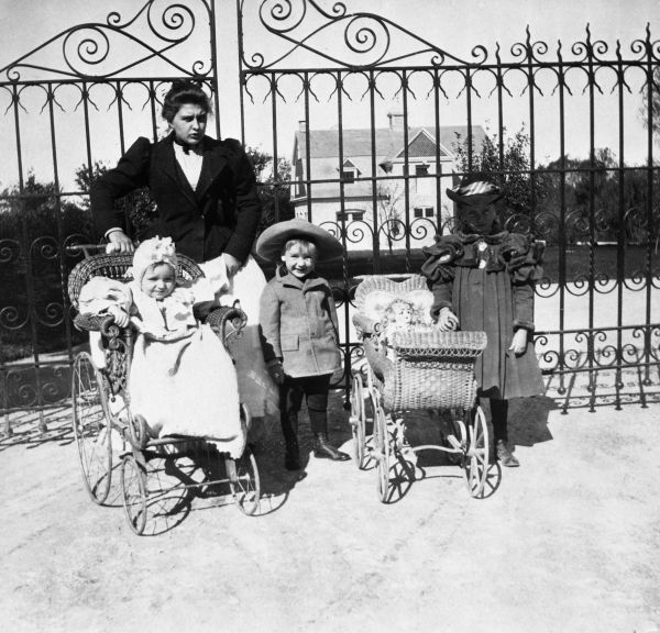 Nursemaid with baby in carriage, boy and girl with doll carriage
