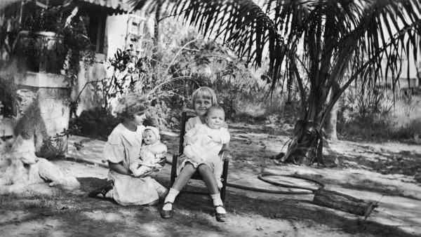 Maizie with doll, and her brother being held by unidentified person