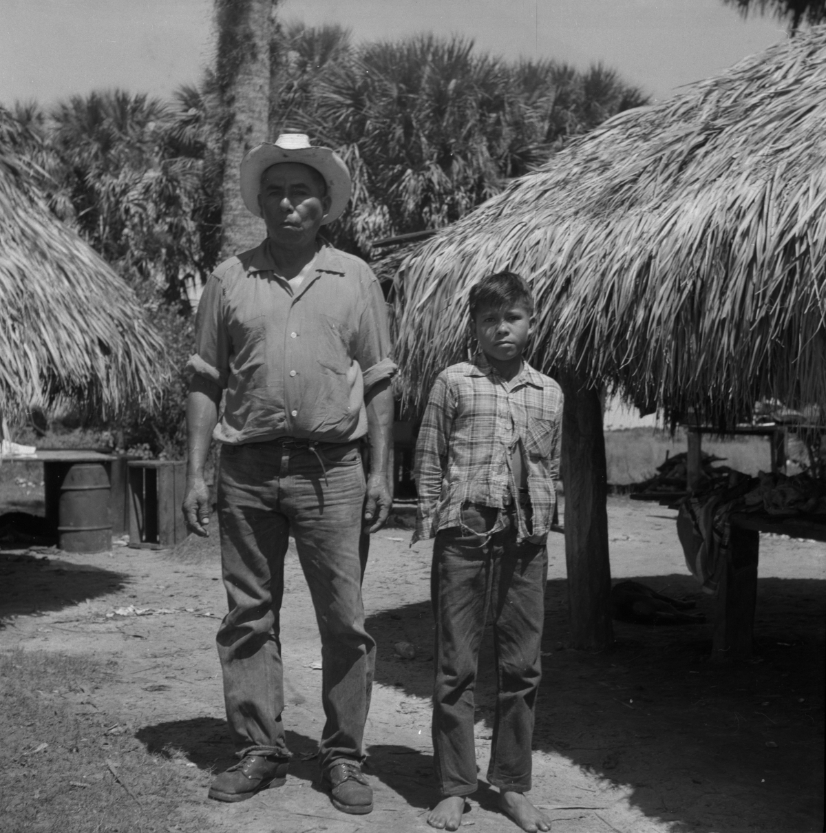 Seminole Indian Frank Shore standing with his son in front of some chickees