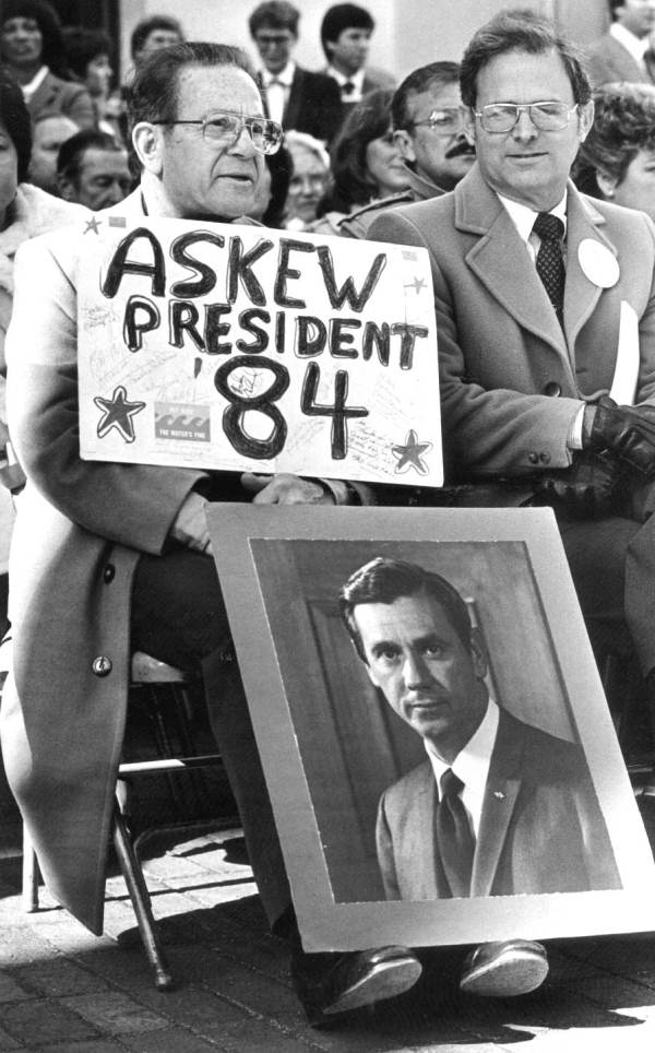 Spectator holding a sign and a picture supporting former Florida Governor Askew.