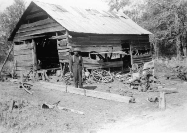 Blacksmith Thomas Raines standing near shack