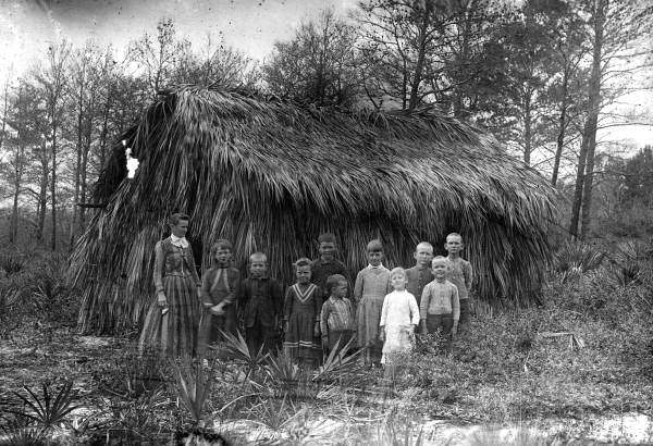 Class assembled in front of a thatched one-room school building