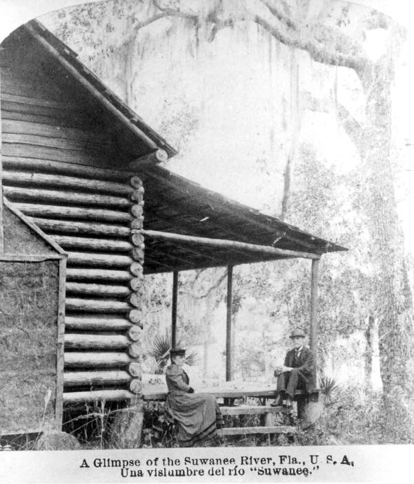Married couple sitting on porch of log cabin by the Suwannee River.