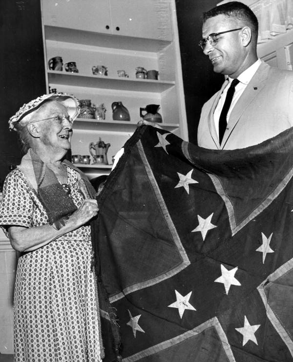 Secretary of State Tom Adams holding up Confederate Army battle flag with Mrs. E.A. Hayden - Tallahassee, Florida.