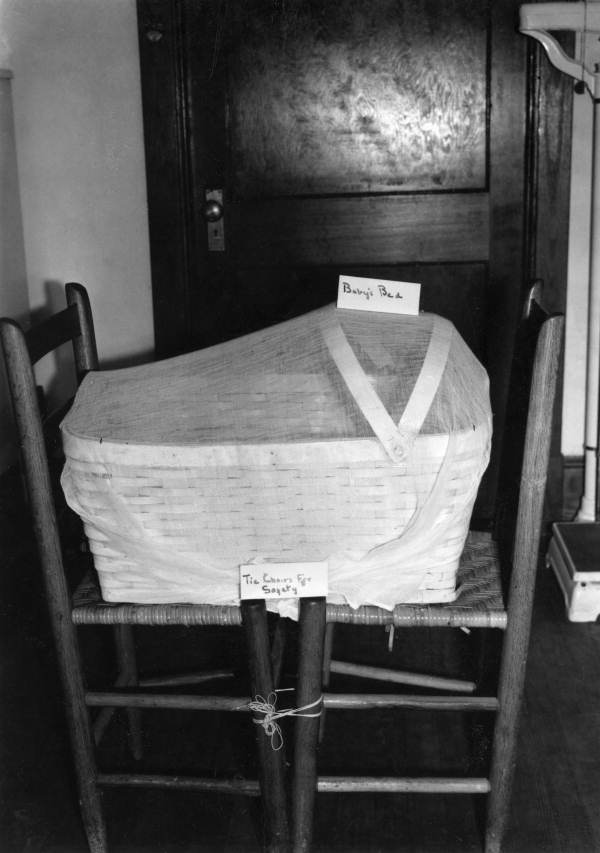 View showing a baby's bed with mosquito net sitting atop two chairs tied for safety.