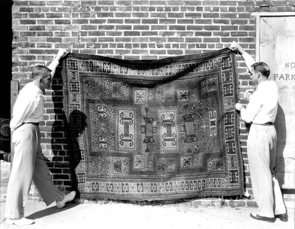 Two men holding up a persian rug.