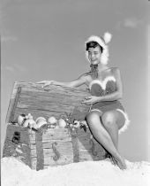 Gloria Howard dressed in Christmas outfit sitting on a chest of fruit