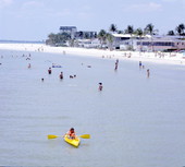 Young man kayaking by people enjoying the beach - Fort Myers, Florida