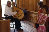 Man playing a bandura as girls look on - White Springs, Florida