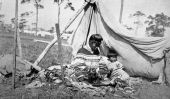 Seminole women sewing under canvas shelter with child beside her - Florida