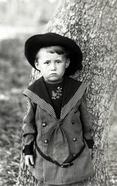 Frowning boy posed in front of tree trunk