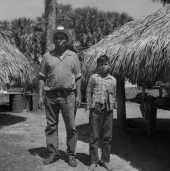 Seminole Indian Frank Shore standing with his son in front of some chickees