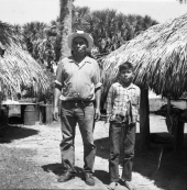 Seminole Indian Frank Shore standing with his son in front of some chickees