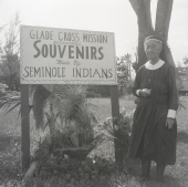 Deaconess Harriet Bedell standing in front of the Glade Cross Mission sign