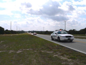 Vintage race cars driving from Sebring Raceway to Sebring for "Taste of the Race" event, escorted by sheriff's vehicle..