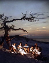 View of group gathered around a bonfire at the beach.